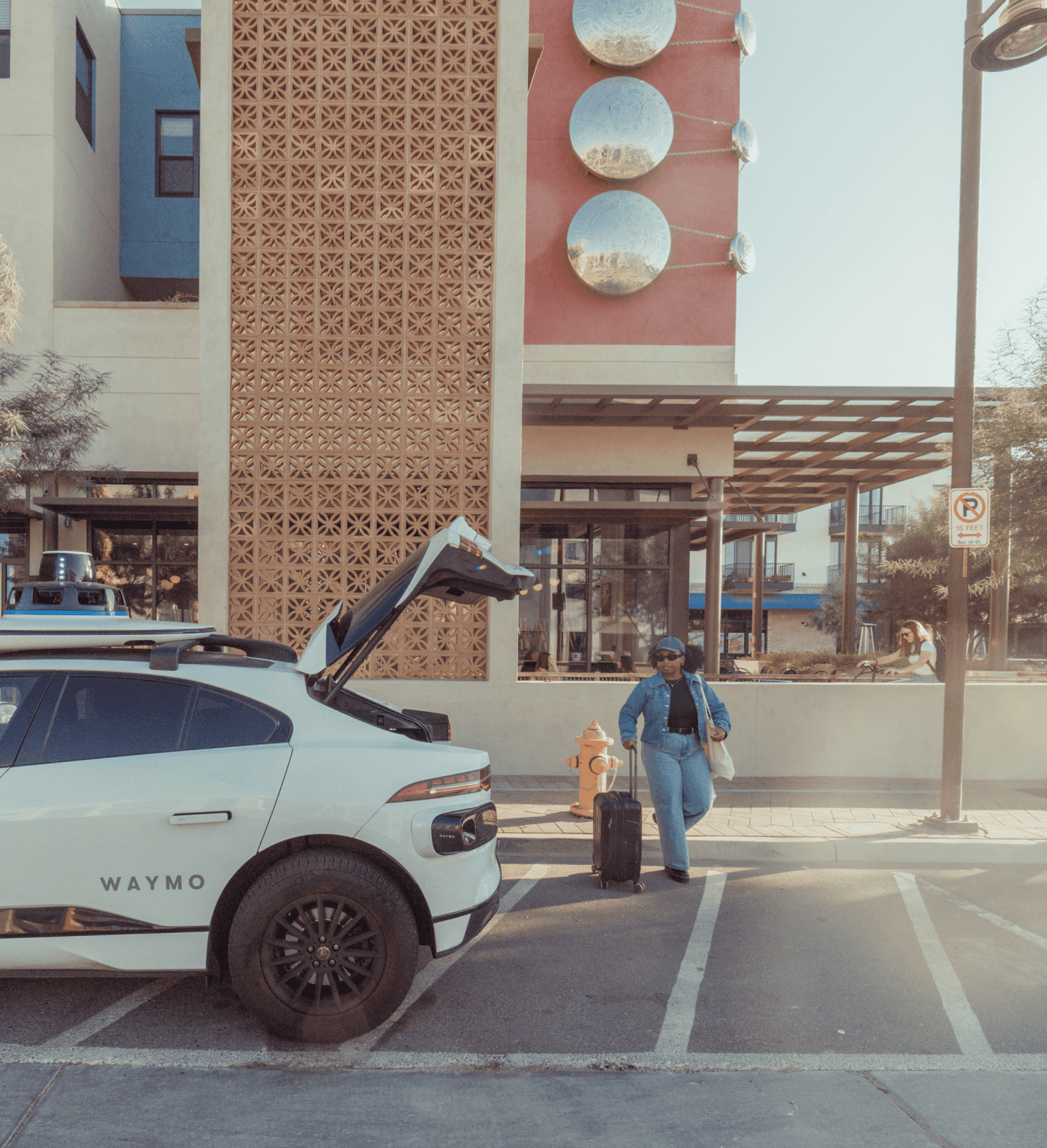 Waymo with trunk open while woman with luggage prepares to get inside