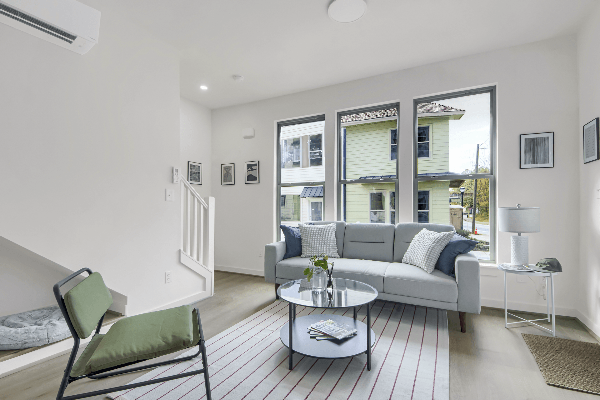 Spacious living room with gray sofa, green accent chair, round glass coffee table, and tall windows with neighborhood view at 1070 Dill Ave
